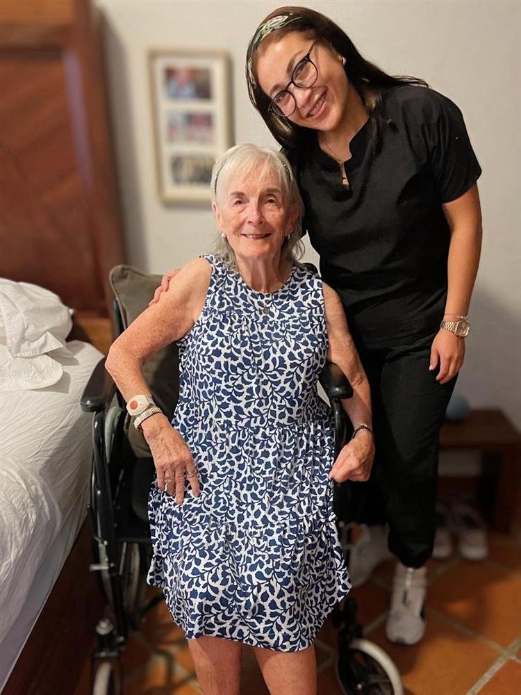 Paciente en silla de ruedas junto a su cuidadora, ambas sonriendo