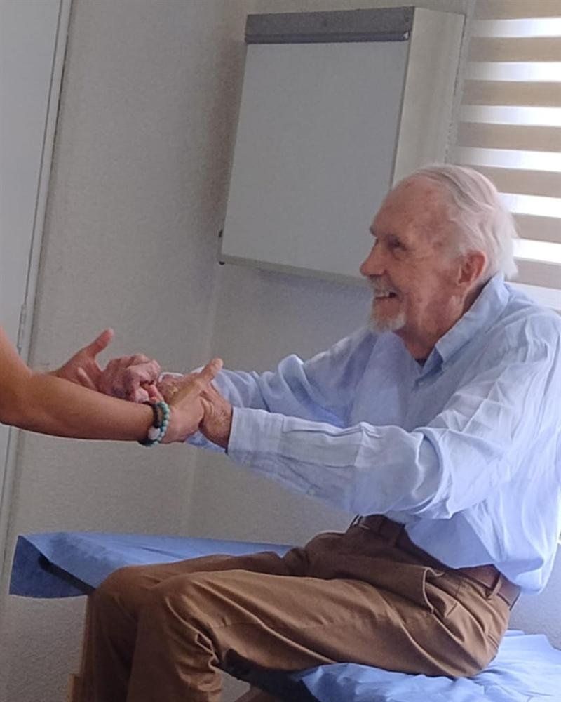 Paciente sonriendo mientras su terapeuta lo toma de las manos durante un ejercicio
