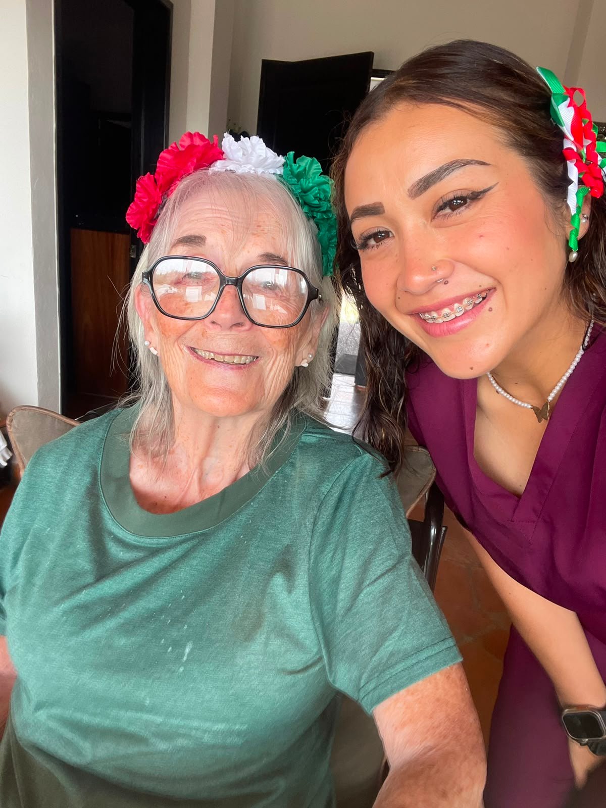 Paciente y cuidadora sonriendo juntas, con adornos tricolores